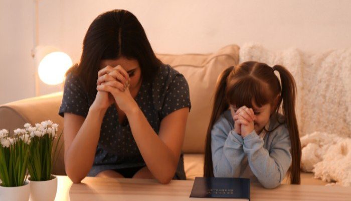 Mãe e filha orando com uma Bíblia na mesa (Foto: Canva Pro)