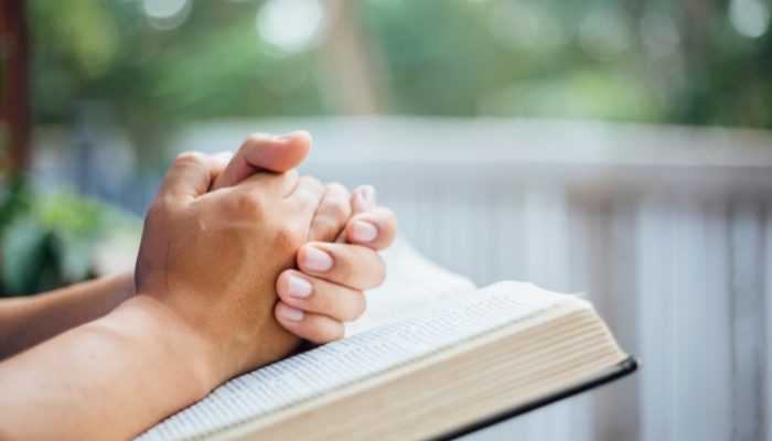 Mãos postas sobre uma Bíblia (Foto: Folha Gospel/Canva)